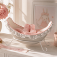 Bild in Galerie-Betrachter laden, Das Bild zeigt eine zarte Belly Bowl aus einem Babybauch Gipsabdruck in Cremefarben mit rosa Posamentenborte und feiner Spitzenbordüre entlang des Randes. Die handgefertigte Bauchschale steht auf einem weißen Sockel auf einer Kommode in einem liebevoll eingerichteten rosa-cremeweißen Kinderzimmer. In der Belly Bowl liegen eine rosa Strickdecke sowie kleine Babysöckchen, wodurch die dekorative und praktische Nutzung der Bauchschale als Erinnerungsstück sichtbar wird - Atelier Body - pArts