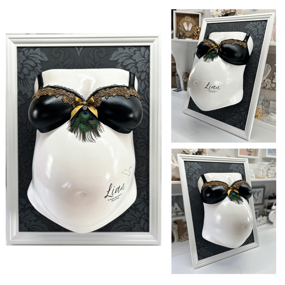„Bilderrahmen mit schwarzer Ornamenttapete und restauriertem, veredeltem Babybauch-Gipsabdruck, weiß lackiert, verziert mit Spitze, Pfauenfedern, Schwarz-Gold-Design, Sternzeichen und den Geburtsdaten des Babys – professioneller Veredelungsservice für Schwangerschaftsabdrücke. - Atelier Body - pArts