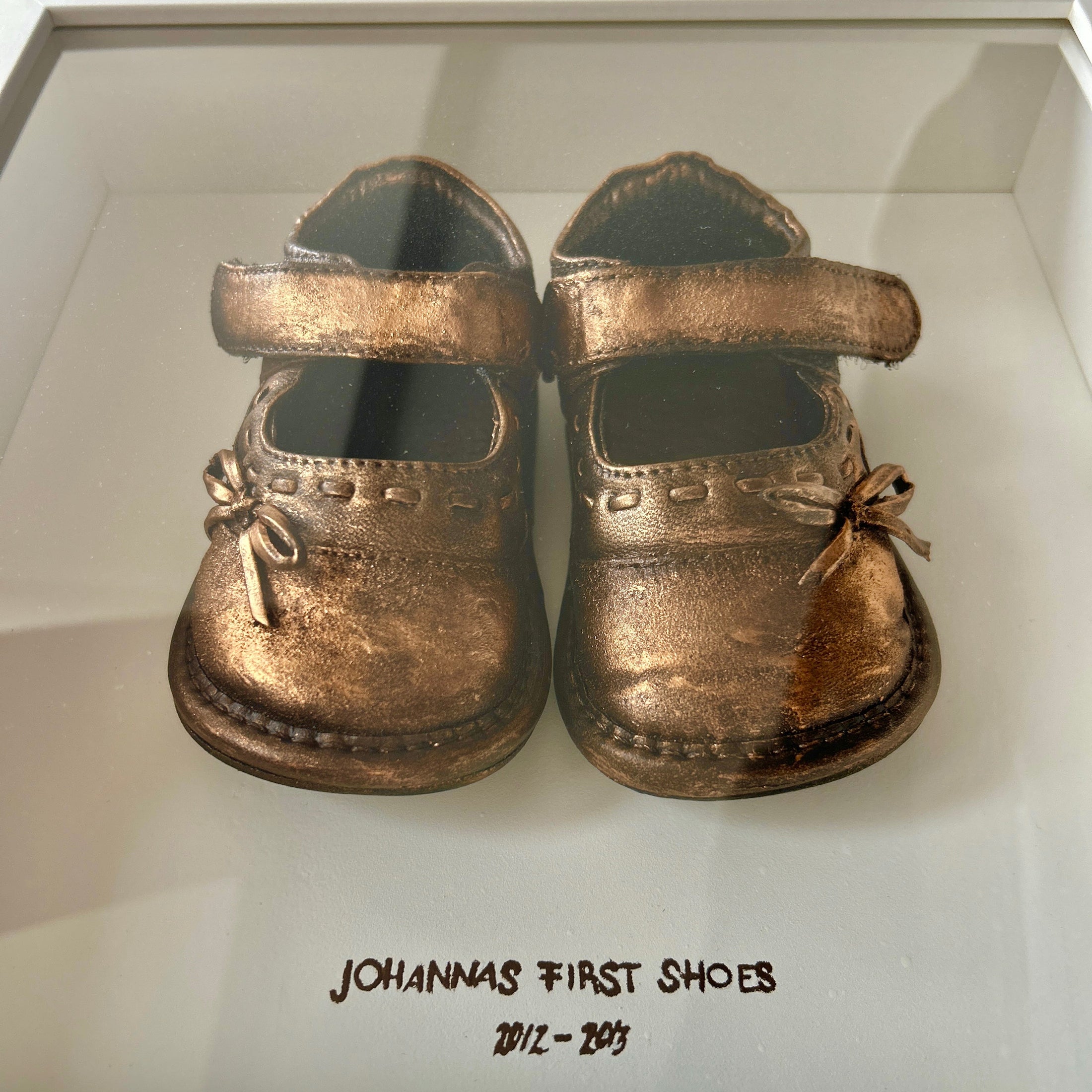 Personalisierter Erinnerungsrahmen mit den ersten Kinderschuhen, veredelt in Gold, Silber oder Bronze, handgefertigt im Atelier Julia Schulze.