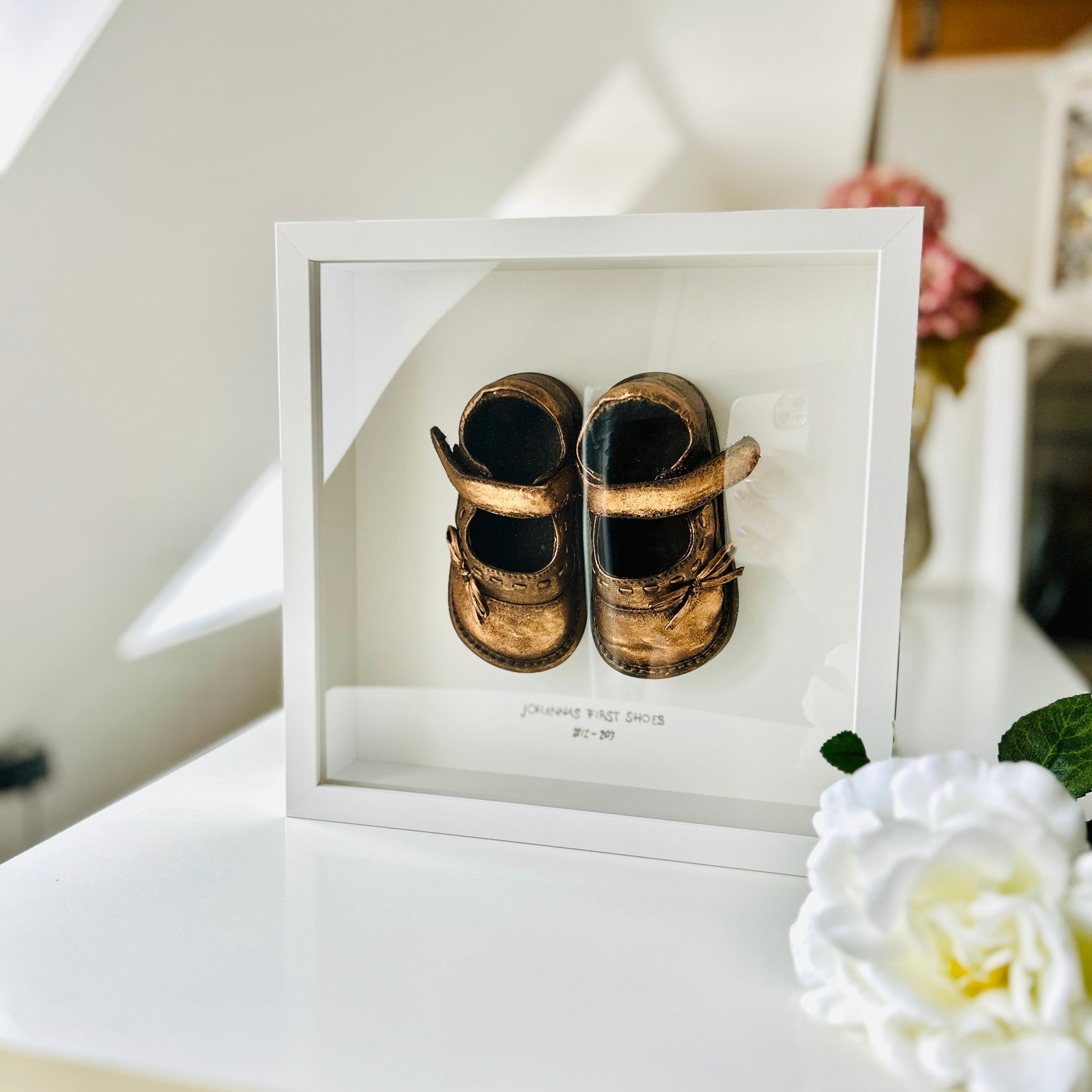 Babyandenken im weißen Rahmen mit bronzefarbenen Babyschuhen, liebevoll handveredelt und personalisierbar mit Name und Jahreszahl. Ein schönes Geschenk zum Geburtstag oder Fest.