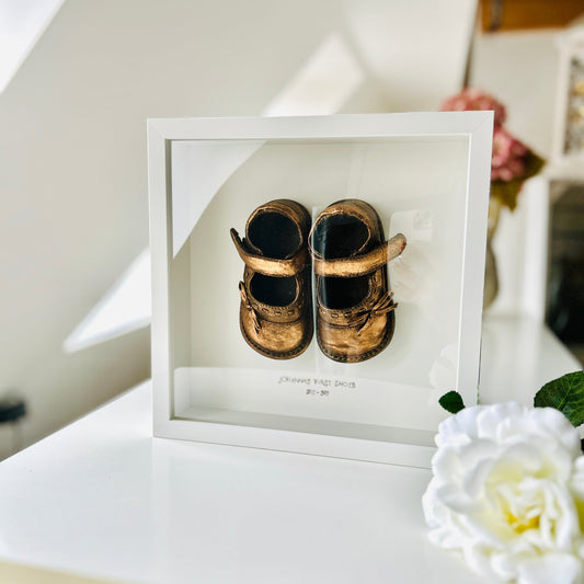 Babyandenken im weißen Rahmen mit bronzefarbenen Babyschuhen, liebevoll handveredelt und personalisierbar mit Name und Jahreszahl. Ein schönes Geschenk zum Geburtstag oder Fest.