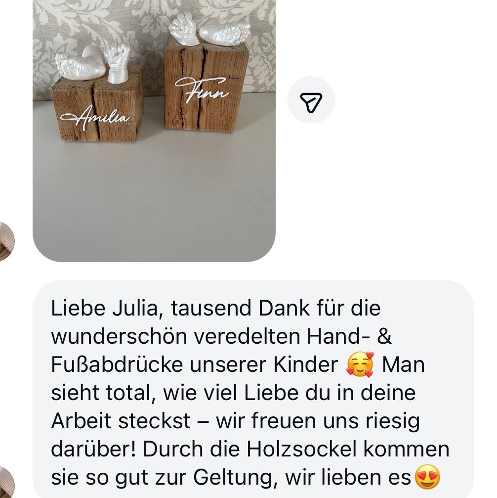 Das Bild zeigt elegante 3D-Babyhand- und Fußabdrücke in Silber-Perlmutt auf handgefertigten Fachwerkholzsockeln mit personalisierten Namensgravuren. Ergänzt wird das Foto durch eine liebevolle Kundenrezension der Mama, die ihre Freude und Dankbarkeit über das emotionale Erinnerungsstück ausdrückt. Die detailreichen Abdrücke fügen sich harmonisch in das stilvolle Wohnambiente ein und bewahren die ersten kostbaren Momente des Kindes für die Zukunft. - Atelier Body - pArts