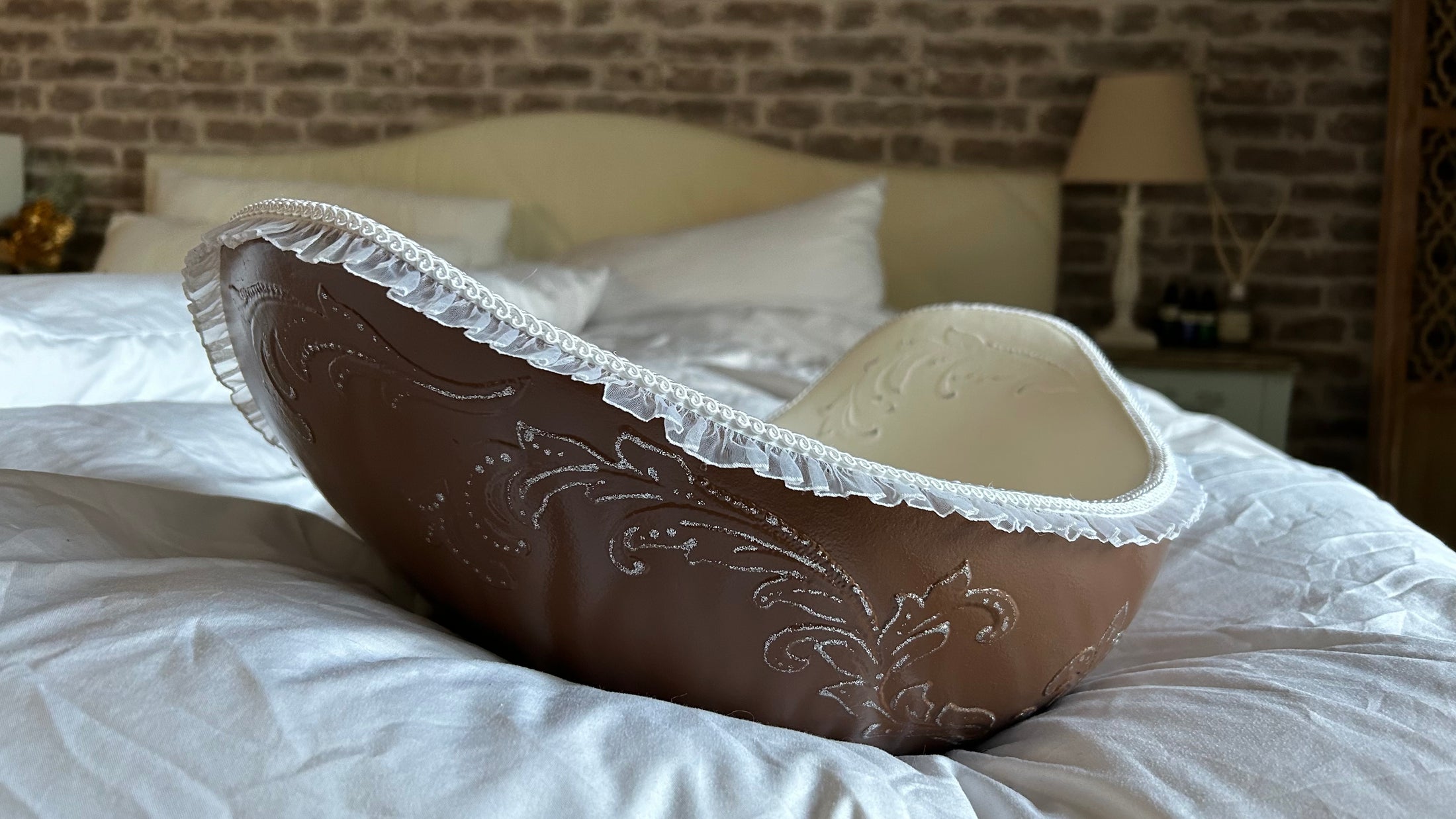 Das Bild zeigt eine edle Belly Bowl aus einem Babybauch Gipsabdruck mit dekorativen Stuckornamenten im Renaissance-Stil. Die Außenseite der handgefertigten Bauchschale ist in Dunkelbraun gehalten, während die Innenseite cremefarben gestaltet wurde. Verziert mit einer weißen Posamentenborte und einer feinen Rüschenbordüre wirkt die Belly Bowl besonders elegant und nostalgisch. Die kunstvoll veredelte Bauchschale dient als stilvolles Wohnaccessoire und persönliches Erinnerungsstück - Atelier Body - pArts